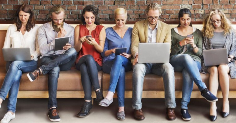 Group of people using eletronic devices seated next to each other in a brown sofa